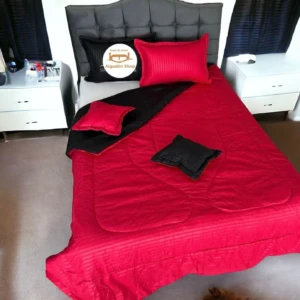 Edredón doble faz rojo y negro, con textura de rayas, sobre cama matrimonial, decorado con cojines.