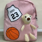 Mochila escolar rosa con apliques de oso de peluche, balón de baloncesto y número 23.