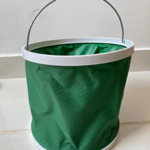 Balde plegable verde con asa metálica y borde blanco, ideal para camping y pesca.