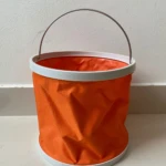 Balde plegable naranja de tela impermeable con aro blanco y asa metálica, ideal para actividades al aire libre.