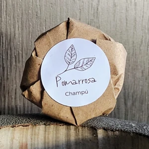 Champú sólido Pqx3U envuelto en papel café con etiqueta redonda de hoja y texto "Pomaarrosa Champú".