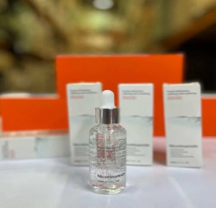 Serum facial Niacinamida en botella de vidrio transparente con gotero, sobre fondo borroso.