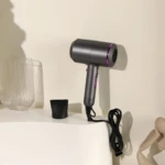 Secador de cabello Nia gris con detalles fucsia, sobre superficie blanca junto a accesorios.
