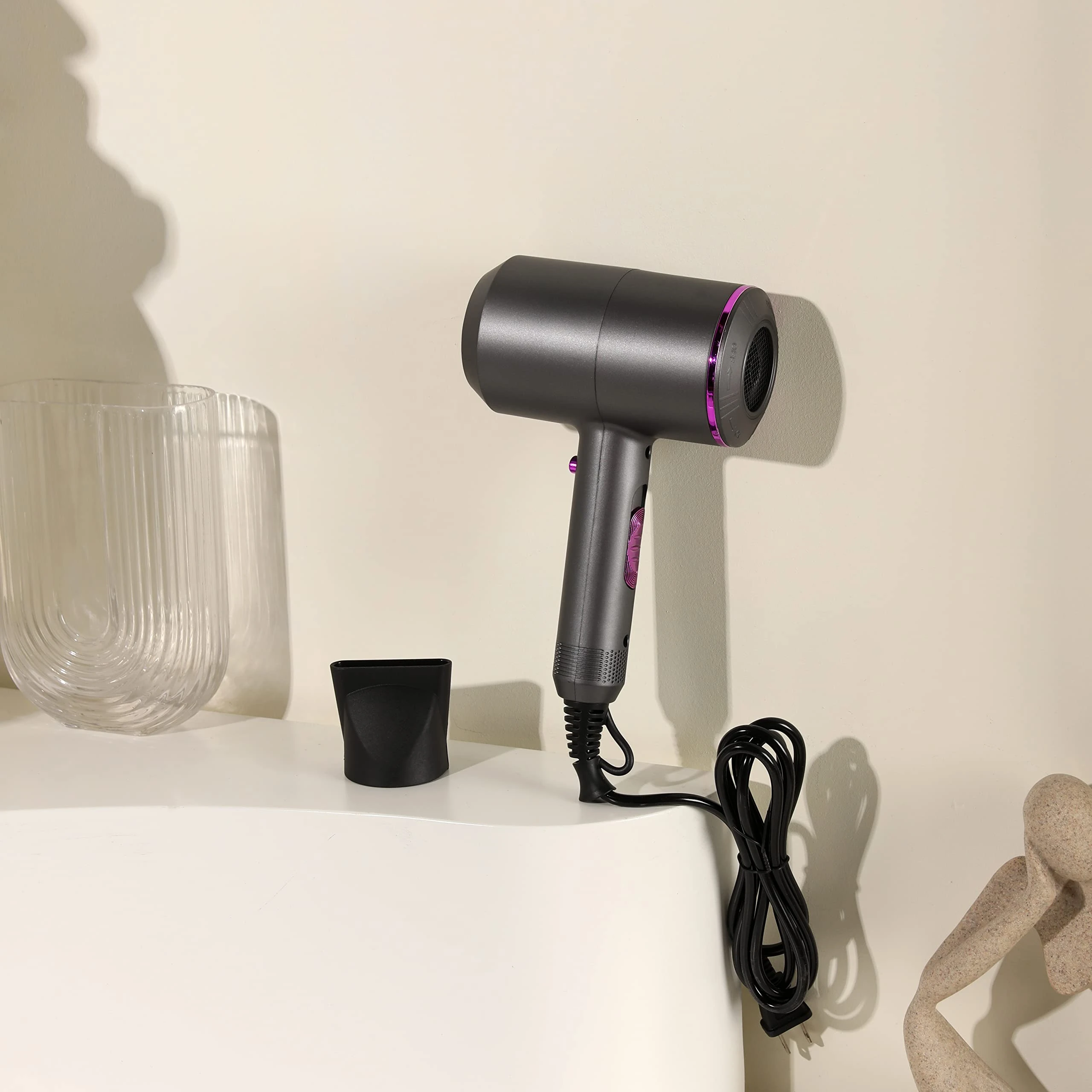 Secador de cabello Nia gris con detalles fucsia, sobre superficie blanca junto a accesorios.