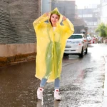 Mujer joven con impermeable amarillo brillante y capucha, parada en calle lluviosa y mojada.