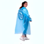 Niña sonriente con impermeable azul brillante tipo poncho, luciendo zapatillas blancas, sobre fondo blanco.