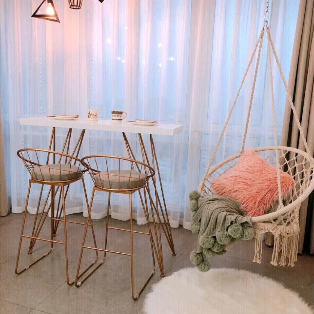 Sillón hamaca de macramé blanco con cojines rosa y verde, ideal para crear un rincón de lectura.