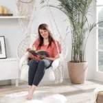Mujer leyendo en silla hamaca colgante de macramé blanco, creando un rincón de relajación acogedor.