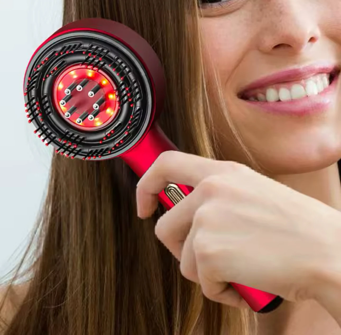 Mujer sonriendo mientras sostiene un cepillo eléctrico masajeador capilar rojo con luz infrarroja y cerdas flexibles para el cuidado del cuero cabelludo.