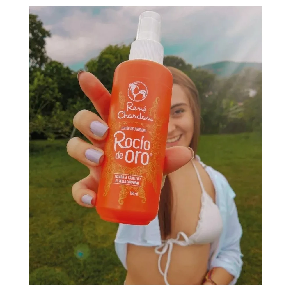 Mujer sostiene una loción aclaradora René Chardon Rocío de Oro de 150 ml en frasco naranja con atomizador, al aire libre sobre un fondo verde natural.