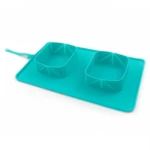 Comedero doble plegable de silicona color turquesa con tapete antiderrames integrado y correa de sujeción, ideal para alimentación de mascotas.