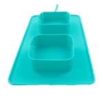 Comedero doble para mascotas de silicona color turquesa sobre tapete antiderrames integrado, diseño plegable ideal para viajes, vista superior angular.