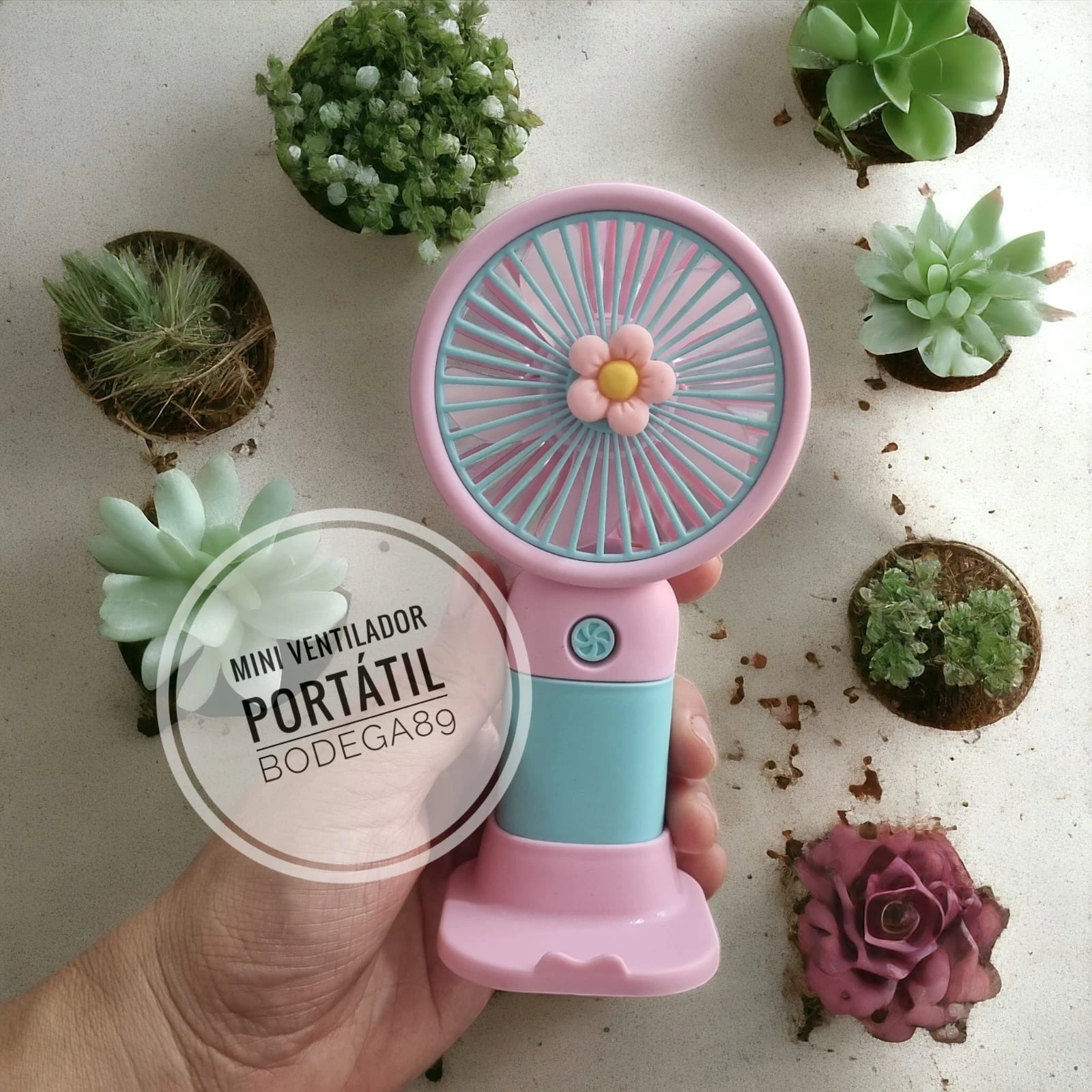 Mini ventilador portátil rosa y azul con forma de flor, ideal para llevar, rodeado de plantas suculentas.