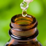 Gota de suero capilar anti-piojos cayendo en frasco ámbar, fondo verde natural.