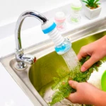 Ahorrador de agua flexible azul y blanco para grifo, lavando ramas verdes en fregadero de acero inoxidable.