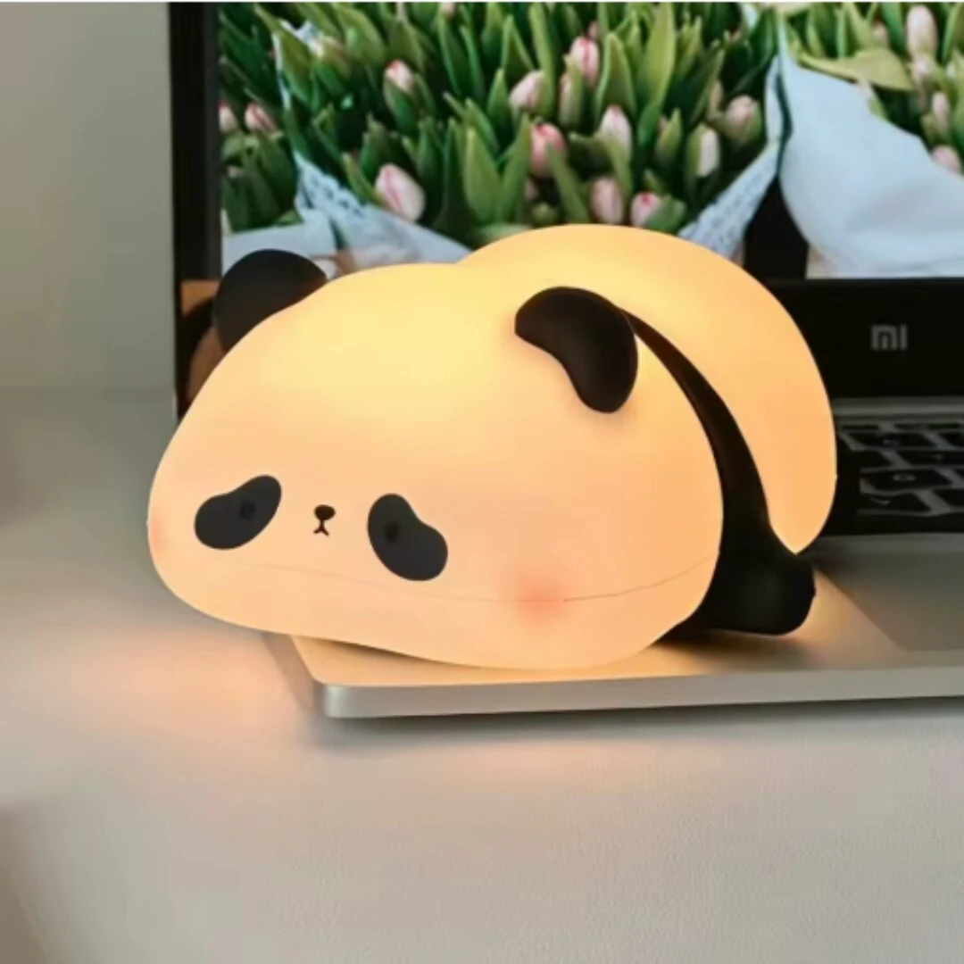 Lámpara de noche táctil en silicona suave con forma de panda, emite luz cálida y está ubicada sobre la base de un computador portátil.
