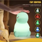 Lámpara de dinosaurio de silicona suave en color verde claro sobre mesa de noche, con una mano activando su cambio de color mediante función táctil.