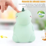 Lámpara nocturna de silicona suave color verde menta con forma de dinosaurio, siendo presionada por un dedo para demostrar su textura flexible y lavable.