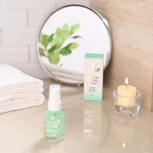 Serum aclararante Reborn 4 en 1 de 30 ml junto a su caja, una toalla blanca, un espejo circular y una vela encendida sobre una superficie reflectante.