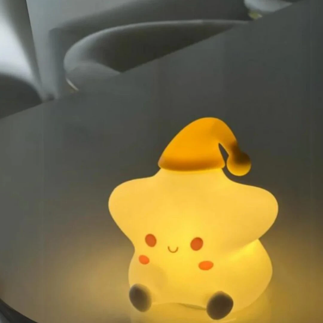Lámpara de noche con forma de estrella de silicona suave en color amarillo cálido, incluye gorro de dormir y pies pequeños, ideal para el descanso.