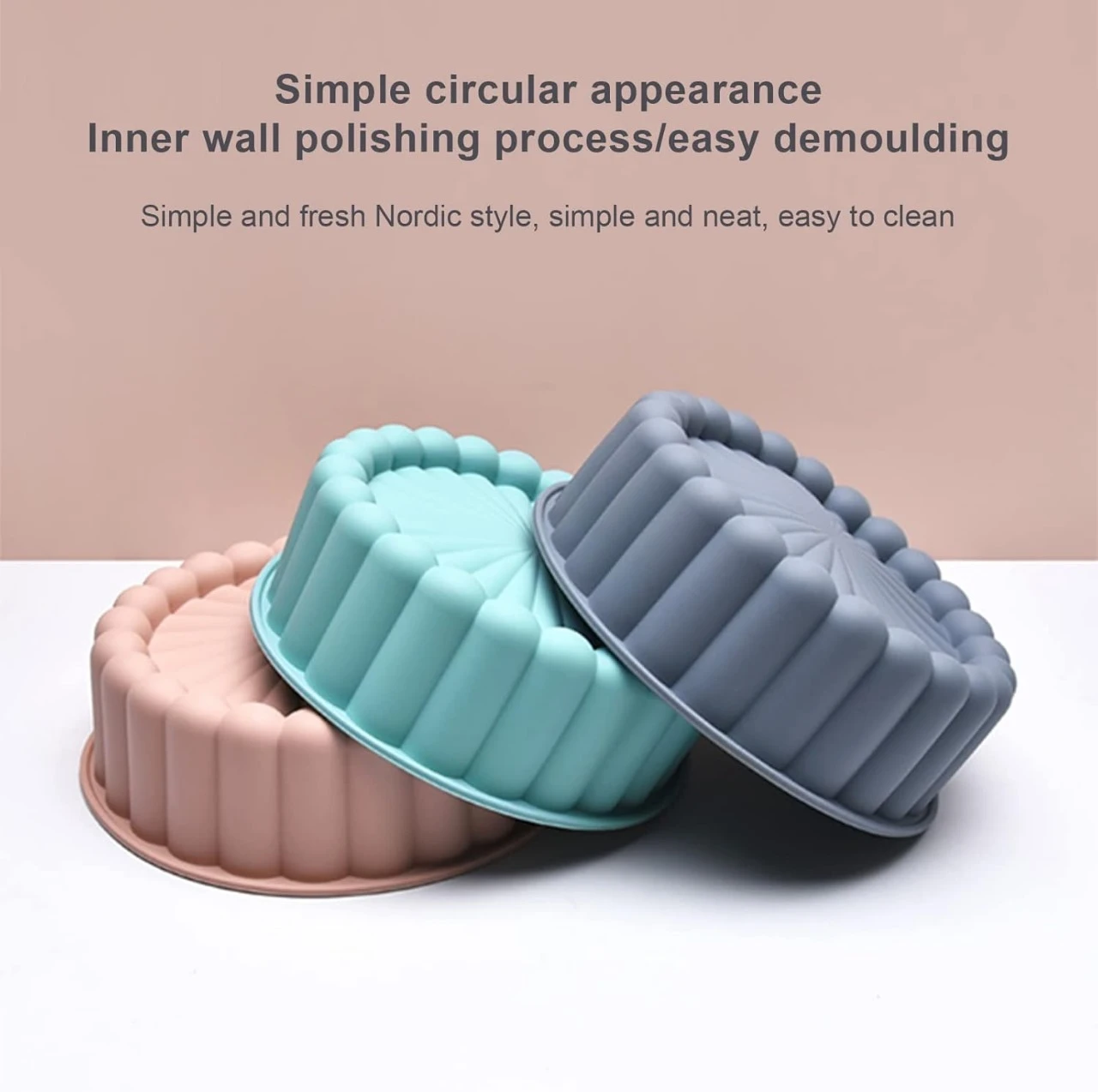 Tres moldes circulares de silicona en colores rosa, turquesa y gris con diseño acanalado para repostería, apilados sobre superficie blanca y fondo beige.