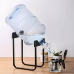 Botellón de agua volcado sobre soporte negro dispensando en tetera de vidrio.