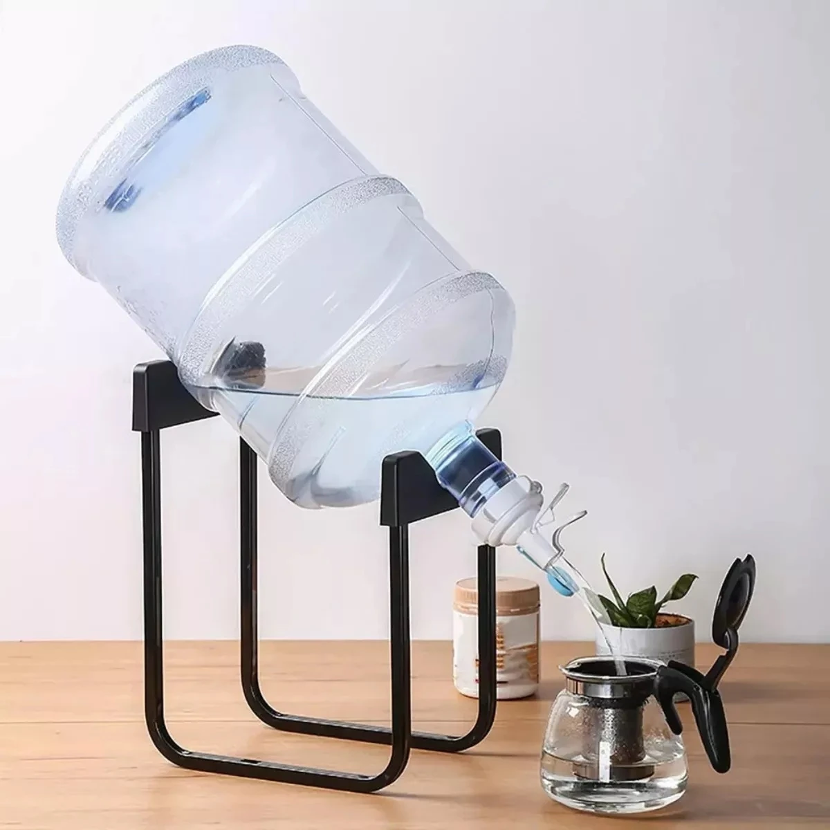 Botellón de agua volcado sobre soporte negro dispensando en tetera de vidrio.