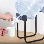 Soporte dispensador negro para botellón de agua, con llave blanca vertiendo agua a taza.