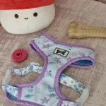 Arnés para perro PetGlam con estampado marino en tonos azules y bordes morados, junto a un juguete de hueso, una pieza circular rosa y peluche de hongo.