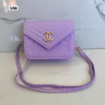 Cartera pequeña morada de cuero sintético con logo Chanel dorado y correa ajustable.