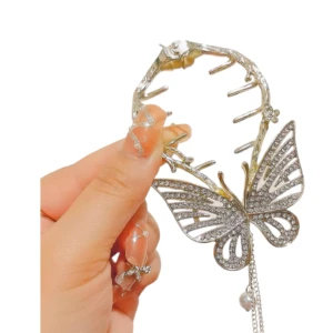 Pinza de cabello dorada con mariposa y pedrería, detalle de perla colgante.