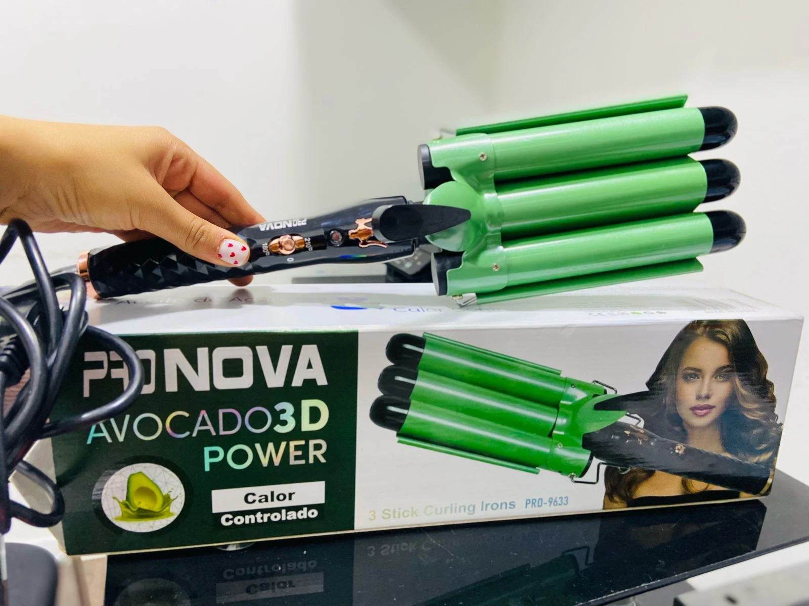 Ondulador de sirena Pro Nova verde de tres barriles sobre su caja original que muestra el empaque y una modelo, sostenido por una mano con manicura.