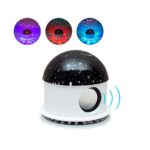 Lámpara proyector de estrellas con altavoz Bluetooth, base blanca con luz inferior y cúpula negra estrellada, incluye tres ejemplos de proyección colorida.
