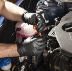 Guantes de nitrilo negro texturizados usados por mecánico para revisar aceite del motor de auto azul.