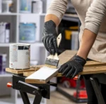 Persona con guantes de nitrilo negros pinta una tabla de madera de blanco con una brocha.
