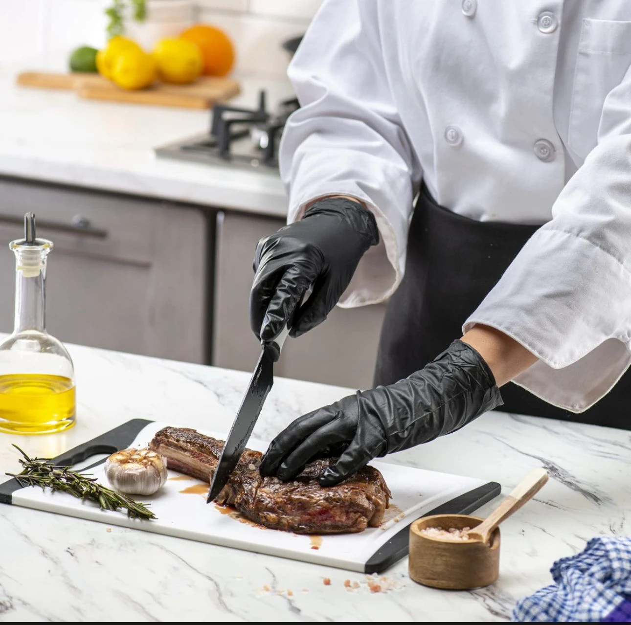 Chef corta filete con cuchillo, vistiendo guantes de nitrilo negro texturizado sobre tabla de corte con romero y ajo.