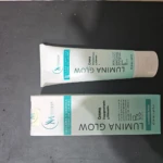 Crema despigmentante Lumina Glow en tubo blanco y su caja protectora, ambos con diseño en tonos verde menta y blanco, contenido neto de 70 ml.