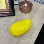 Cepillo masajeador quitapelos Jl02 amarillo brillante, de forma ovalada con dos botones, sobre superficie de madera.