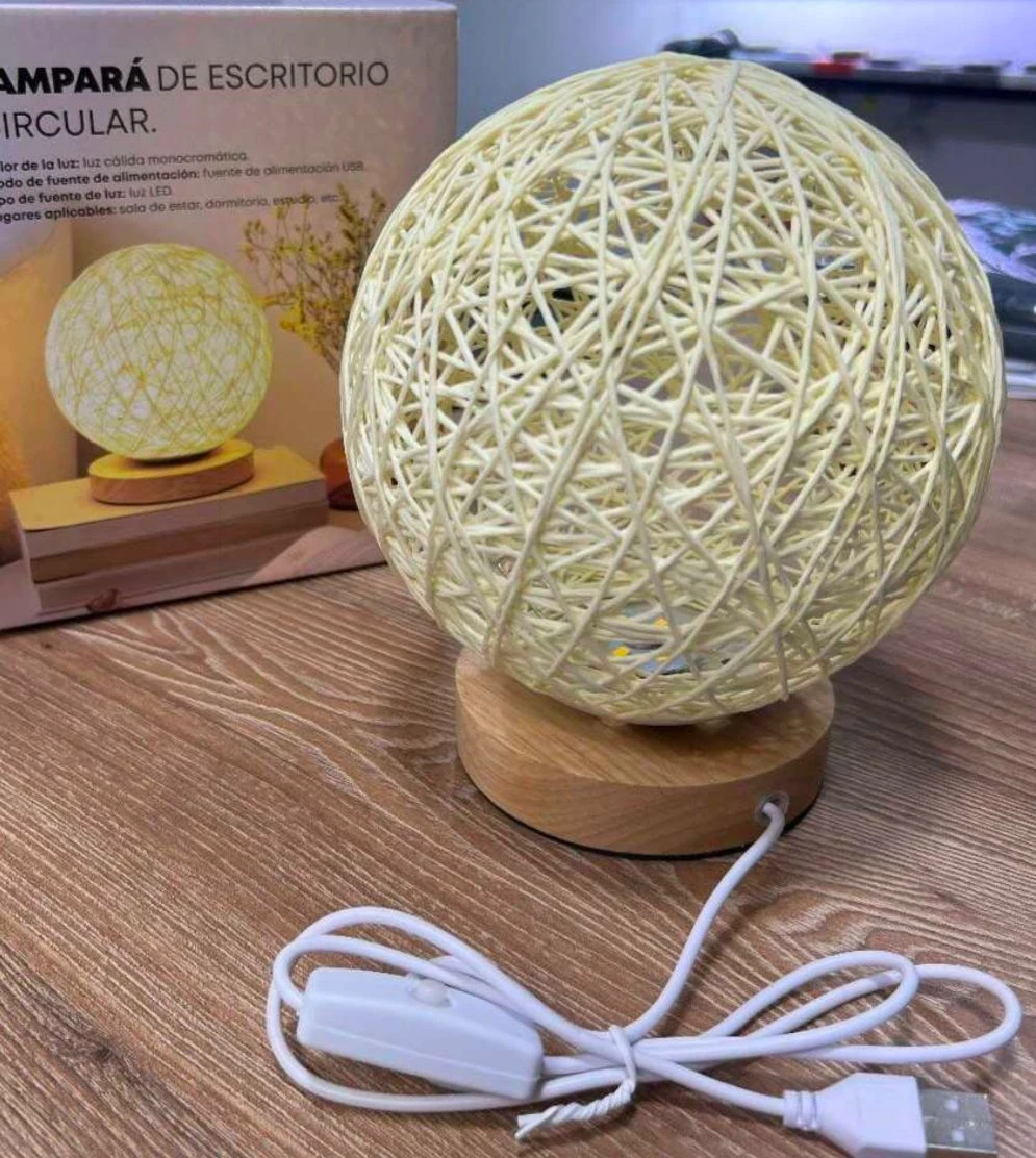 Lámpara de mesa circular con pantalla de hilos entrelazados color crema, base de madera clara, cable USB con interruptor y caja de empaque al fondo.