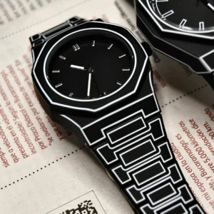 Reloj de pulso estilo caricatura 2D en silicona negra con bordes blancos, diseño geométrico y correa de eslabones sobre fondo de periódico con código QR.