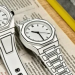 Dos relojes de pulso blancos con diseño tipo caricatura 2D, contornos negros definidos, correa de silicona, sobre papel informativo en superficie madera.