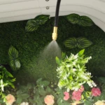 Manguera de riego X de 6 metros rociando agua sobre césped artificial y flores, con accesorio dorado.