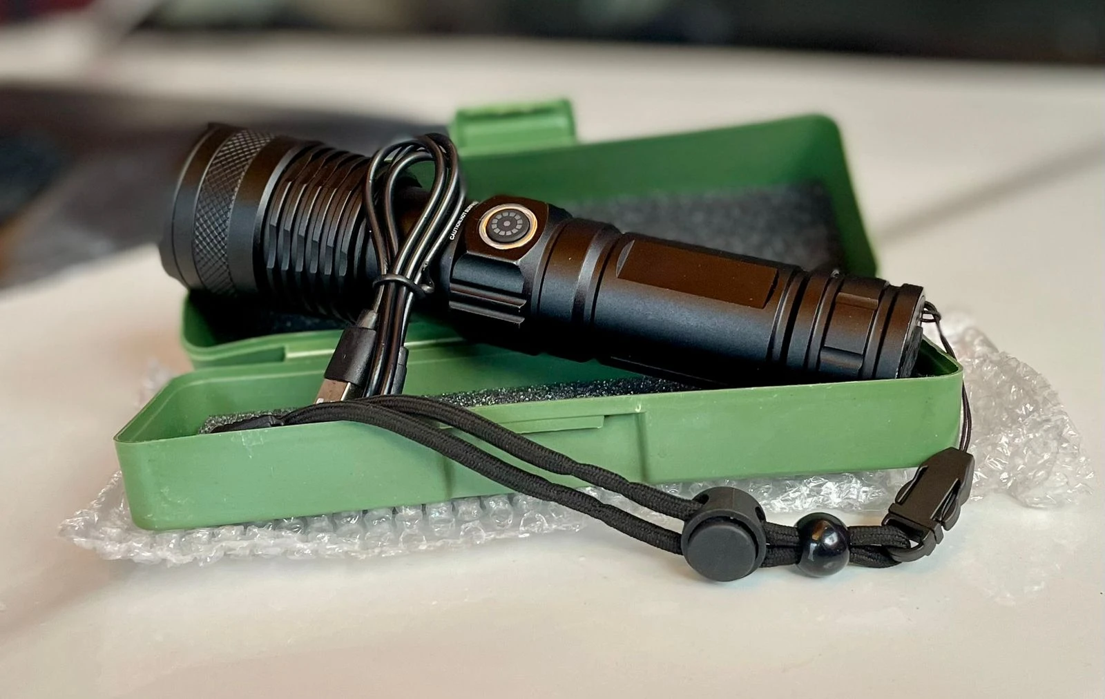 Linterna LED negra recargable de 2500 lúmenes en estuche verde con cable USB.