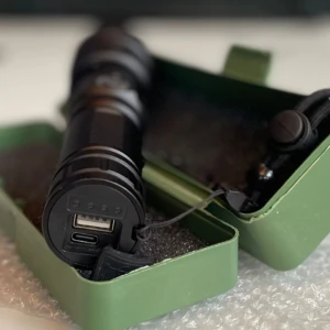 Linterna LED táctica negra recargable con puerto USB y estuche verde.