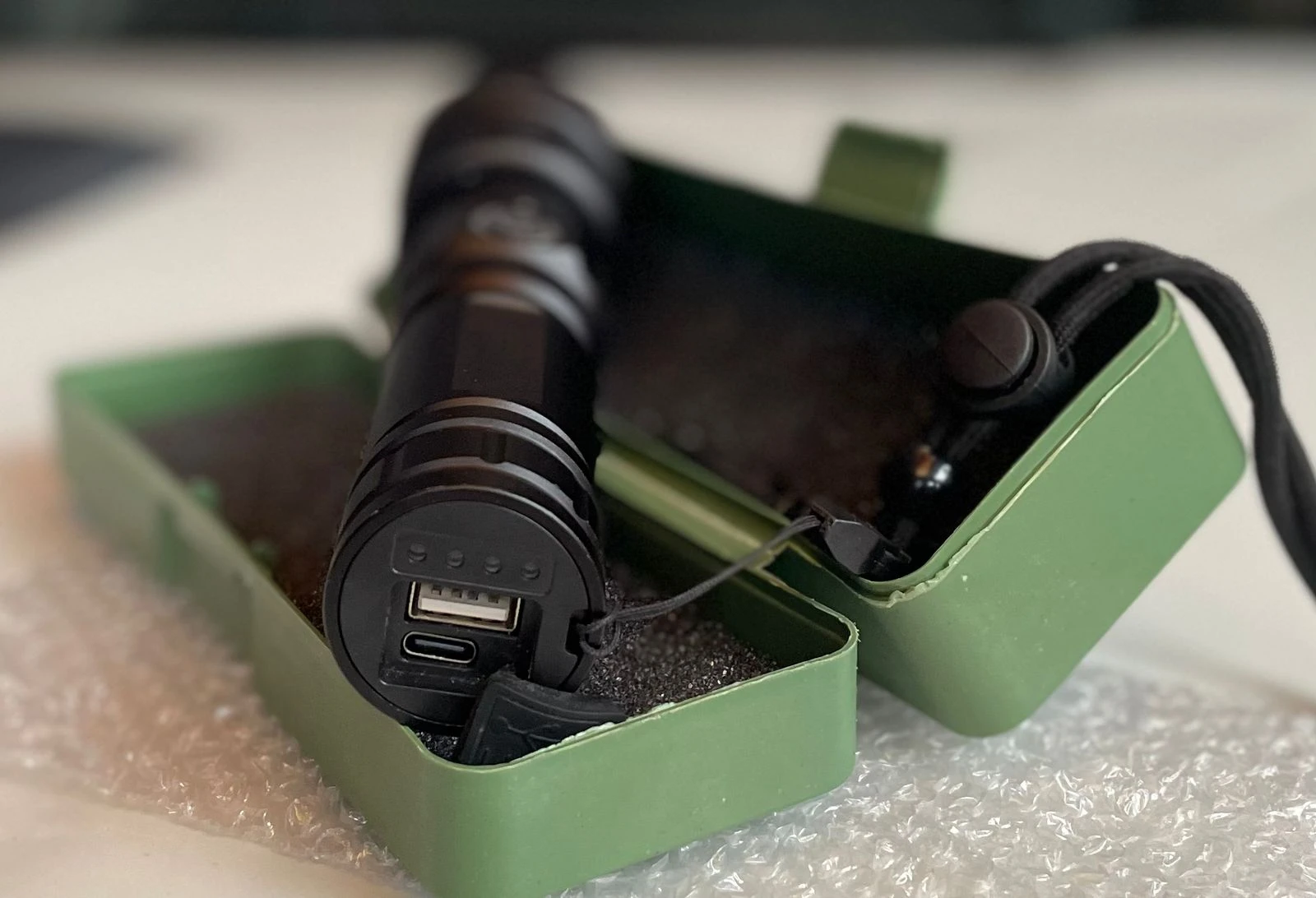 Linterna LED táctica negra recargable con puerto USB y estuche verde.