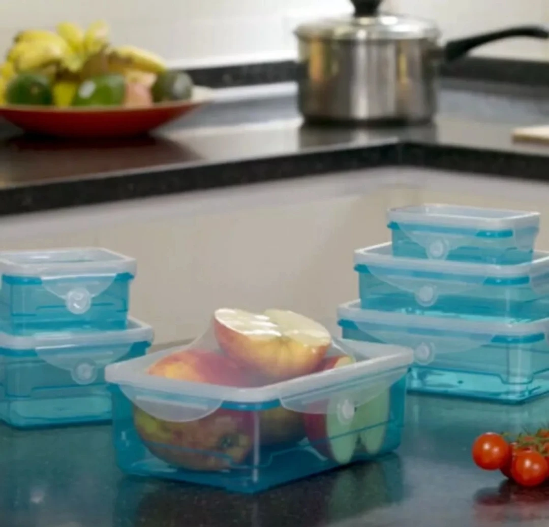 Set de contenedores plásticos azules con tapas de silicona elástica, organizados en la cocina, incluyendo un recipiente con manzanas cortadas frescas.