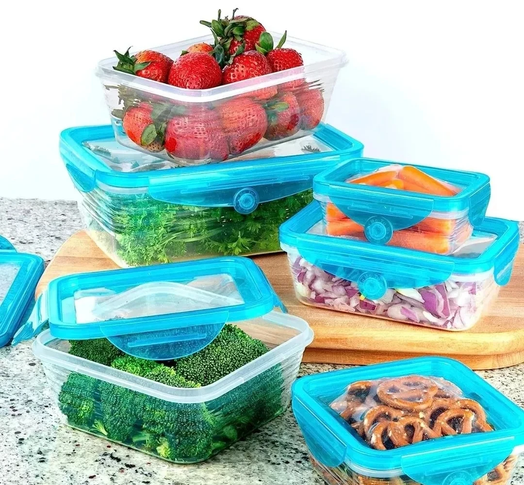 Conjunto de contenedores plásticos transparentes con tapas herméticas azul turquesa, almacenando fresas, brócoli, cebolla, zanahoria y pretzels en cocina.