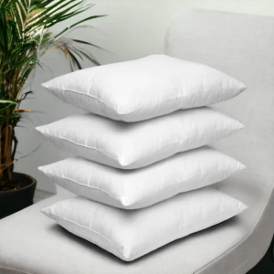 Pila de cuatro almohadas siliconadas de color blanco con acabado suave, dispuestas verticalmente sobre un sillón gris al lado de una planta de interior.