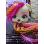 Mascota VIP de juguete con cabeza grande, ojos verdes y cabello largo de colores fucsia y naranja, con un diseño de corazón en su camiseta y maquillaje.