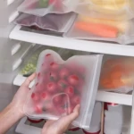 Bolsas Ziploc de silicona translúcidas con tomates rojos dentro, en un refrigerador.